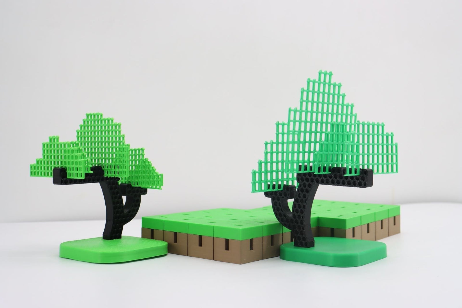 3D‑printed pixel‑style trees and square grass terrain blocks, green‑black tree models on white background.